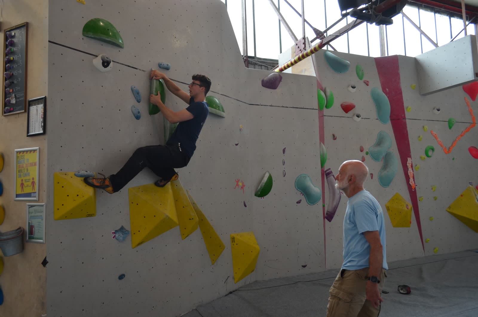 A climber reaching for a hold while a coach watches