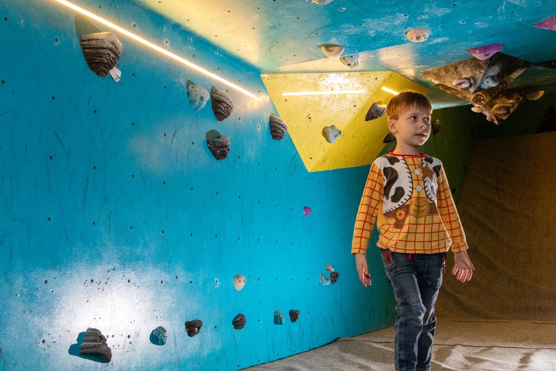 A small boy standing on the mats beside the blue wall