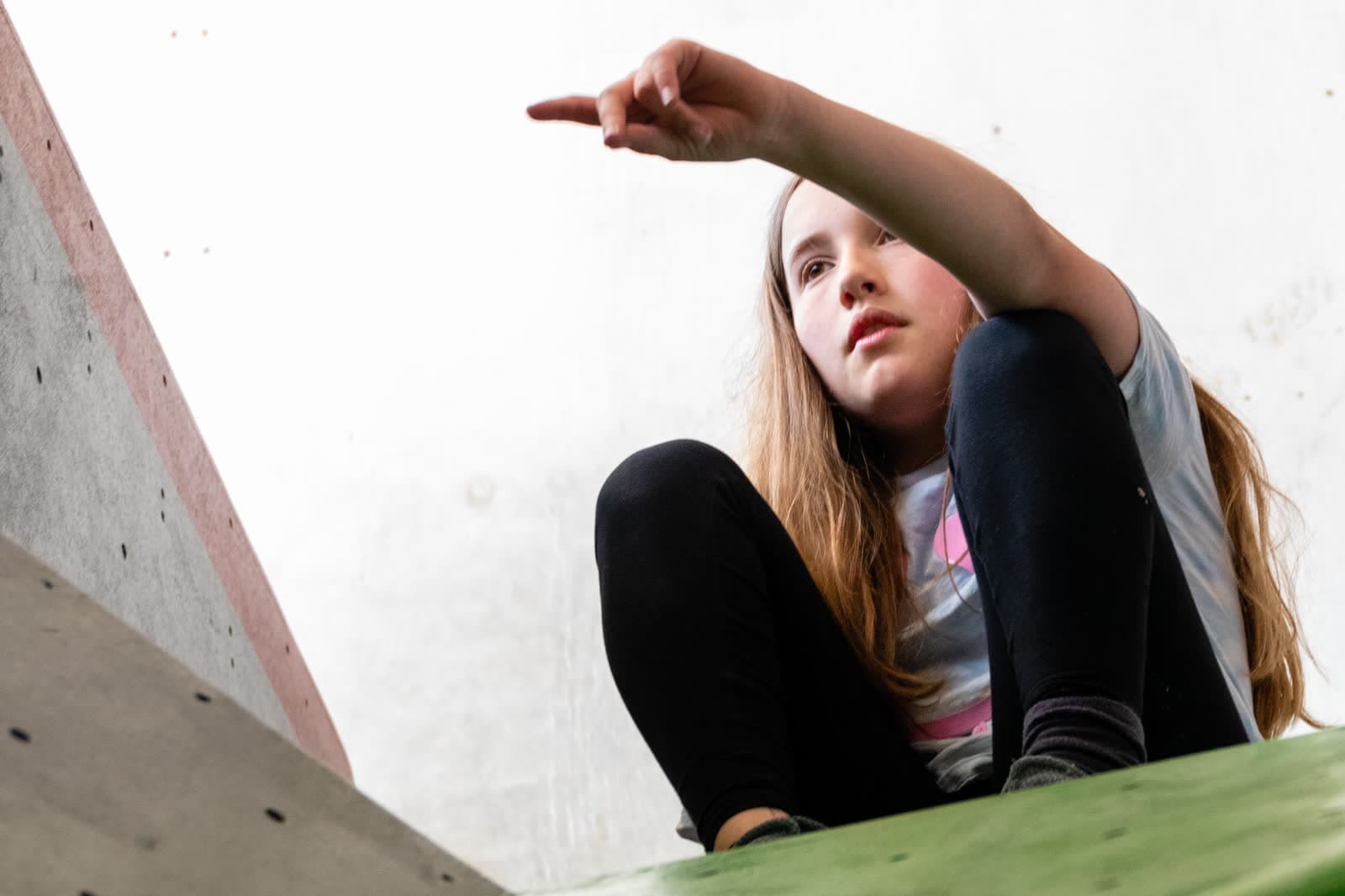 A young climber sitting at the top of the wall, pointing